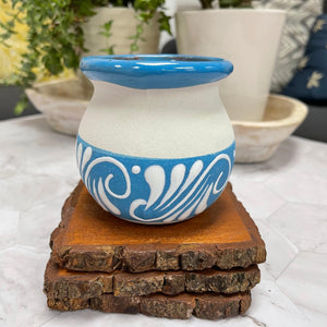 Blue and white ceramic Mexican Clay Tacita candle on top of 3 wooden coasters with plants in the background.