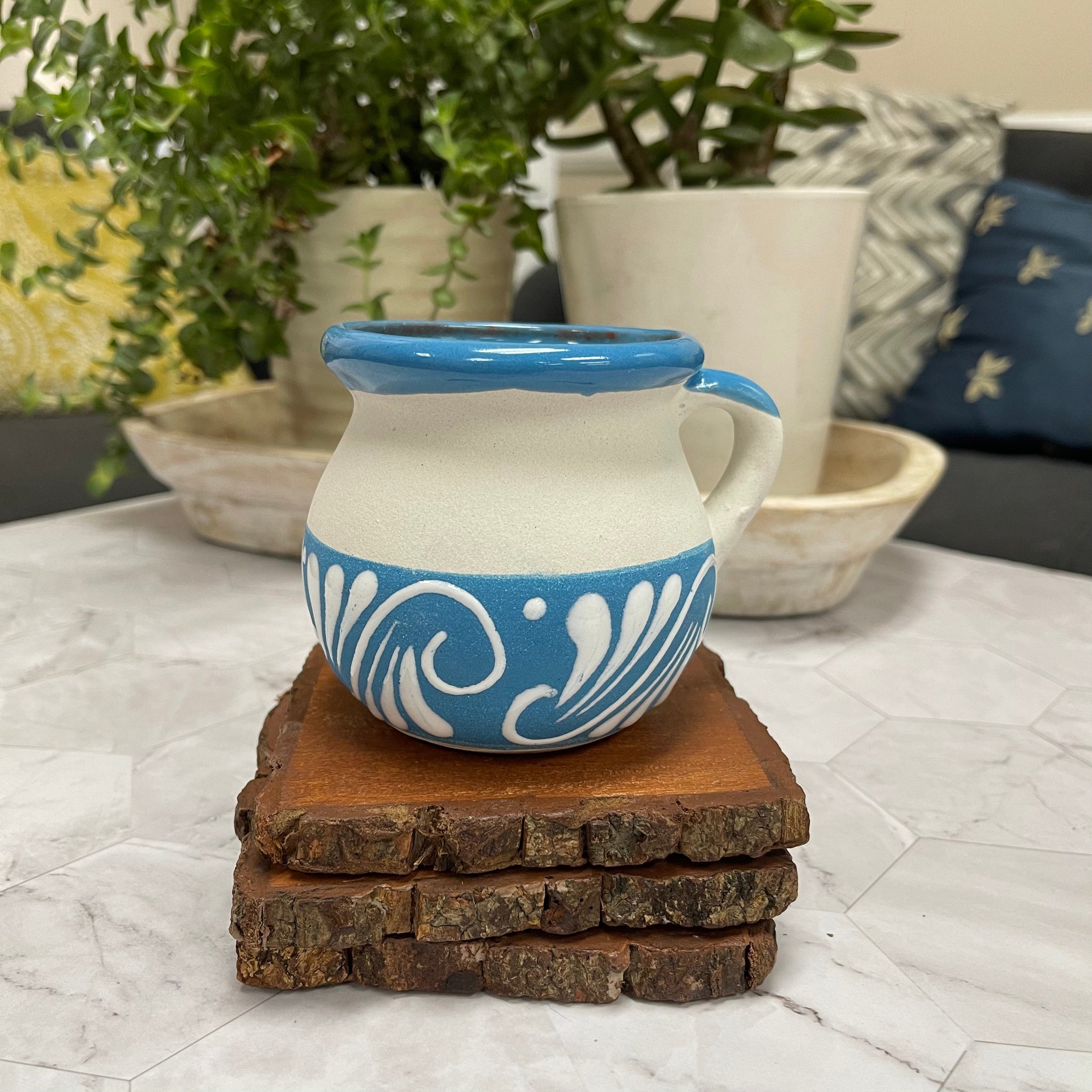 Blue and white ceramic Mexican Clay Tacita candle on top of 3 wooden coasters with plants in the background.