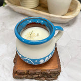Blue and white ceramic Mexican Clay Tacita candle on top of 3 wooden coasters with plants in the background.