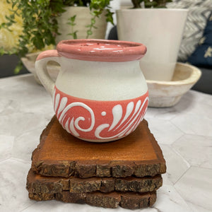 Pink and white ceramic Mexican Clay Tacita candle on top of 3 wooden coasters with plants in the background.