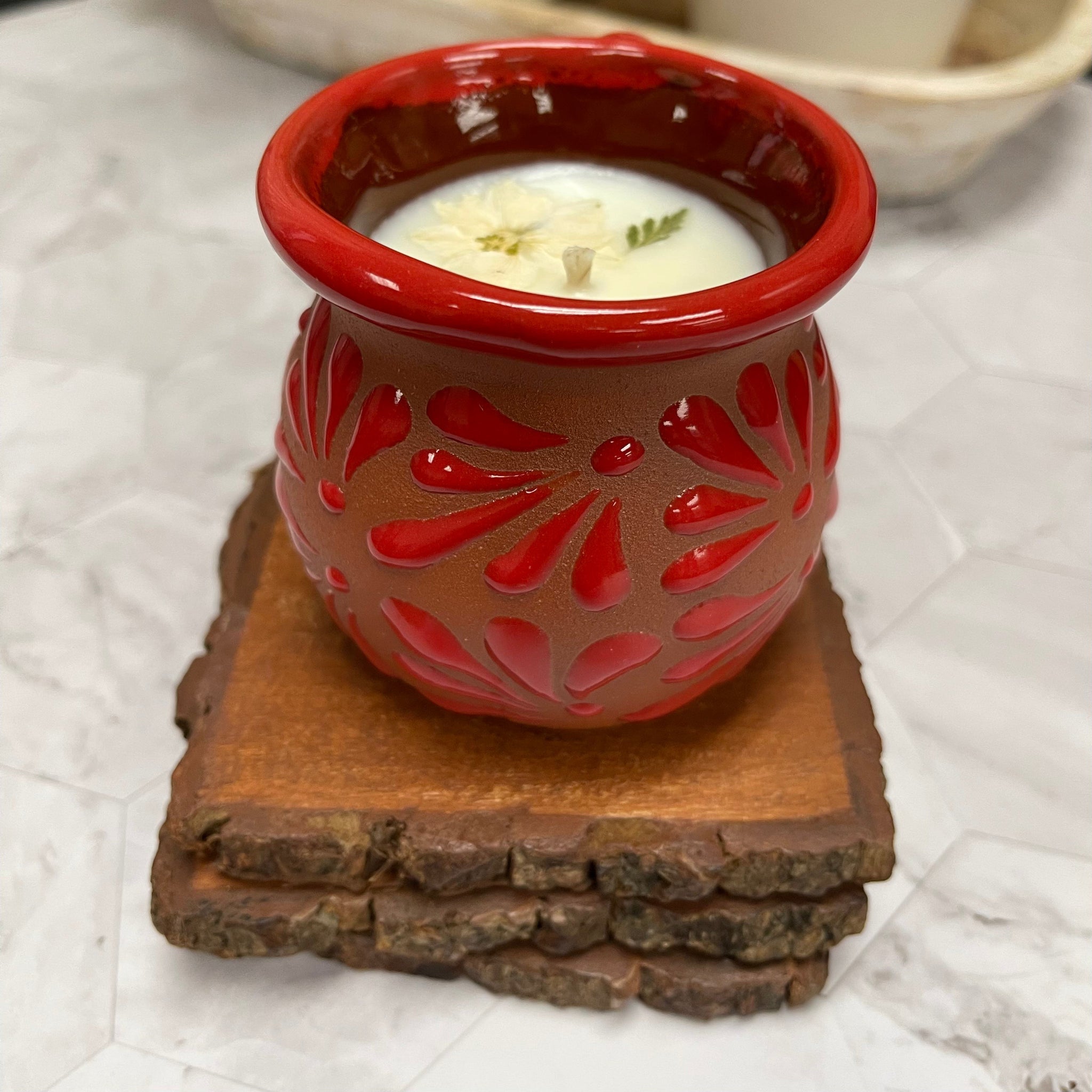 Red ceramic candle holder with floral patterns on top of 3 wooden coasters.