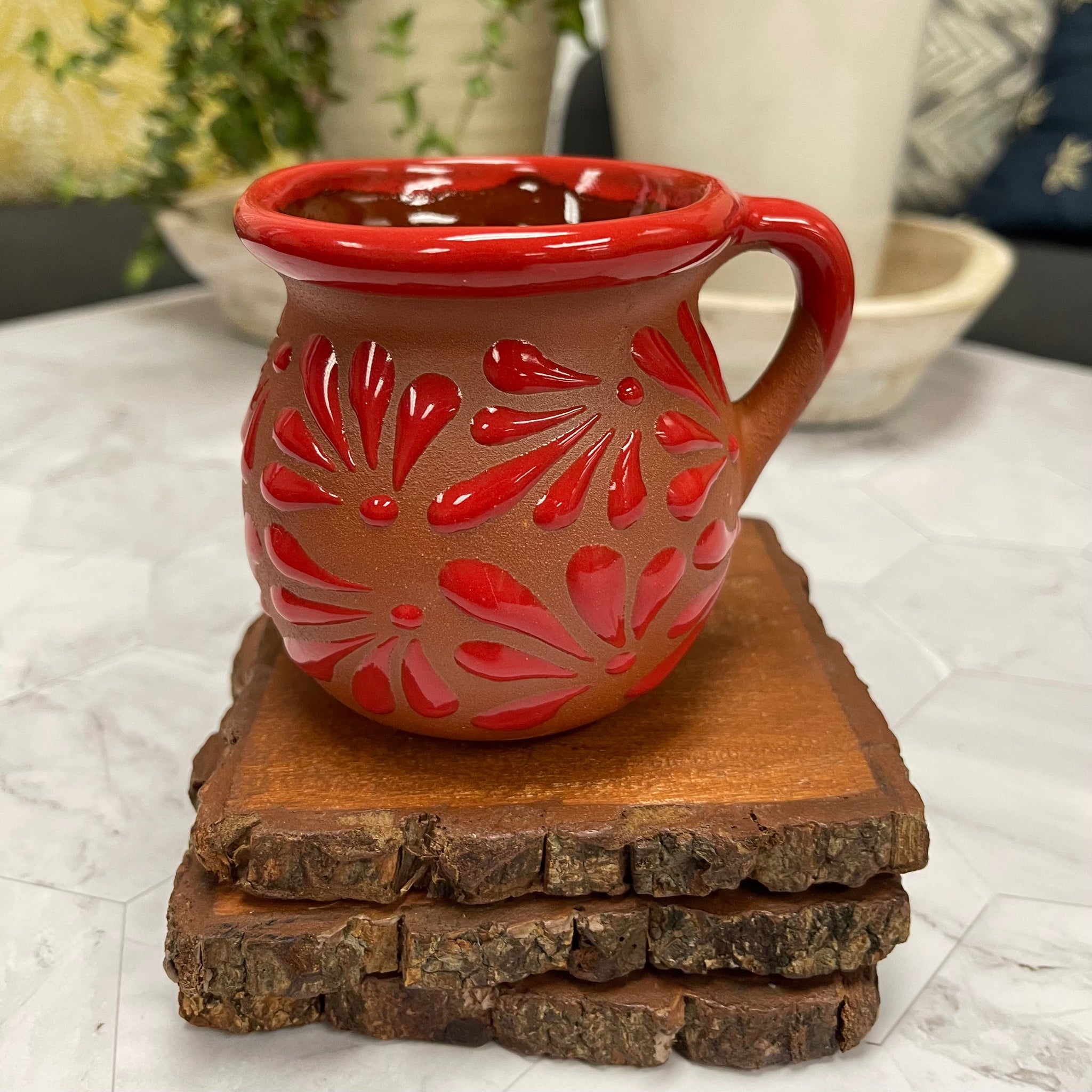 Red ceramic candle holder with floral patterns on top of 3 wooden coasters.