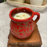 Red ceramic candle holder with floral patterns on top of 3 wooden coasters.