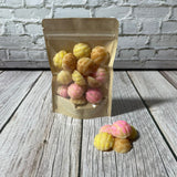A clear packaging bag with multicolored wax melts visible inside, placed on a wooden surface with a few wax melts scattered outside the bag.